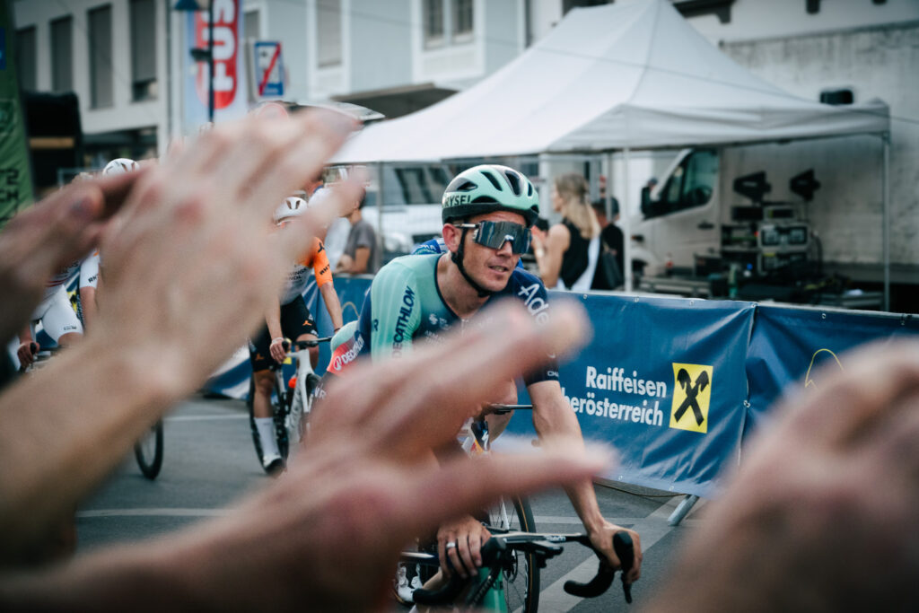 Radrennfahrer im Rennen, im Vordergrund Hände von Zuschauern