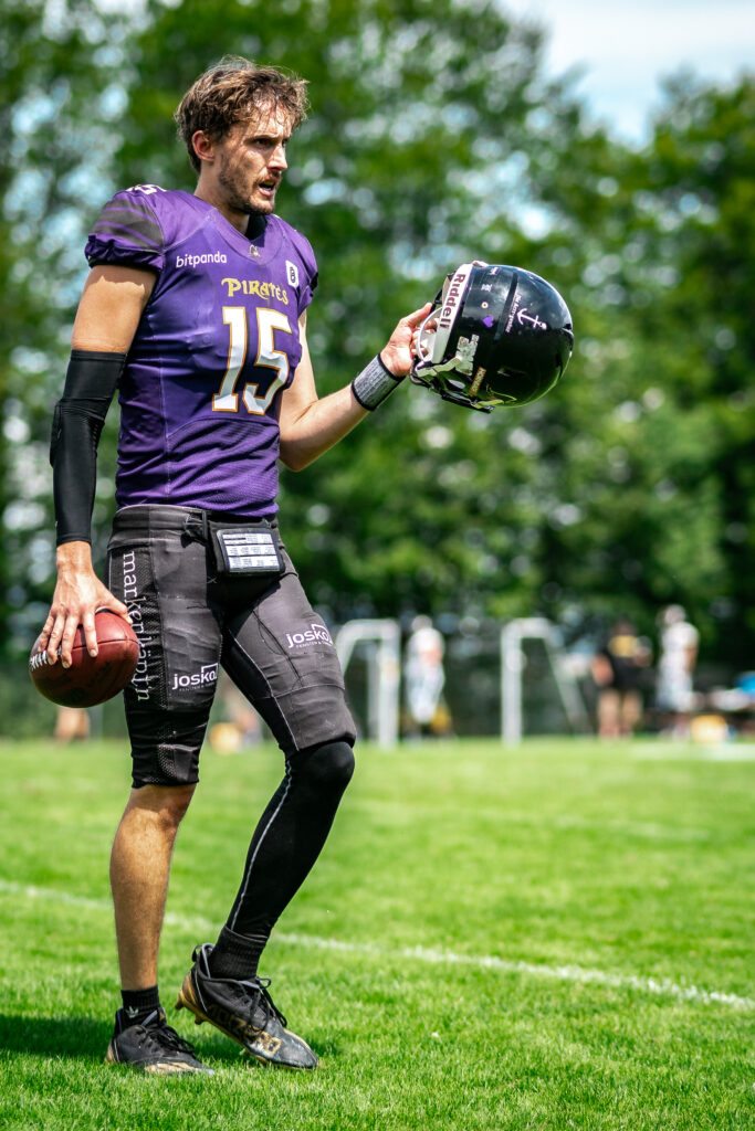 Football-Spieler in violettem Trikot mit Helm in der Hand