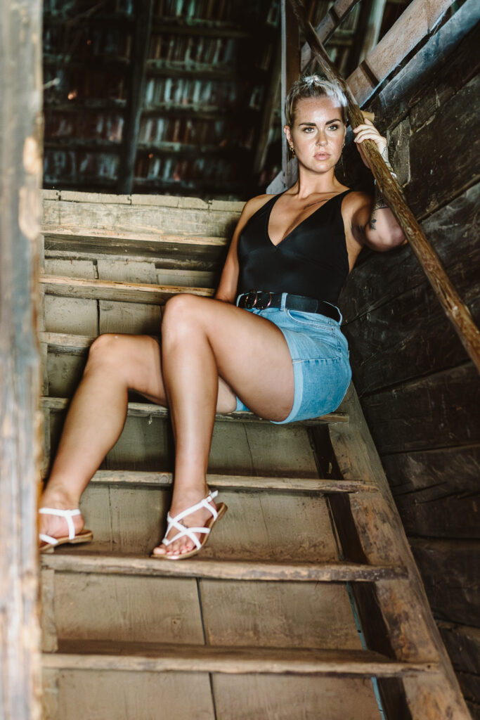 Frau in schwarzem Top und Jeansshorts sitzt auf einer Holztreppe