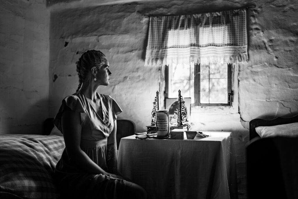 Schwarz-Weiß-Foto einer Frau, die in einer Stube am Fenster an einem Tisch sitzt