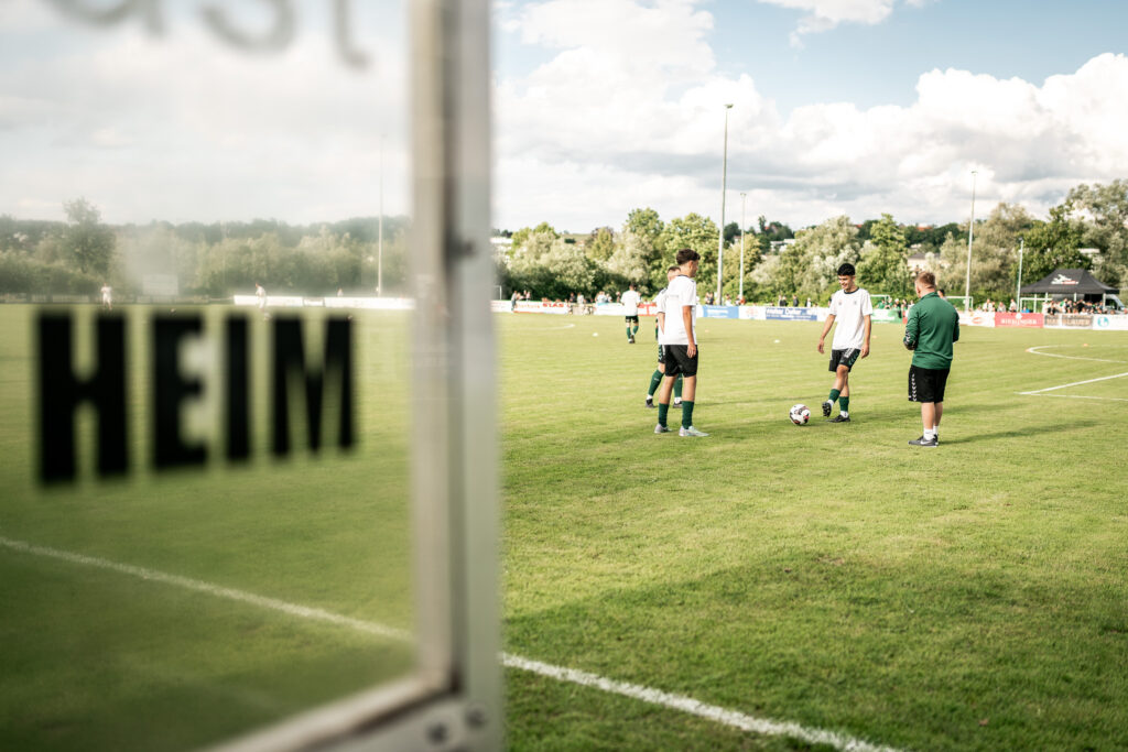 Fußballplatz mit einem Schild “HEIM” am Spielfeldrand