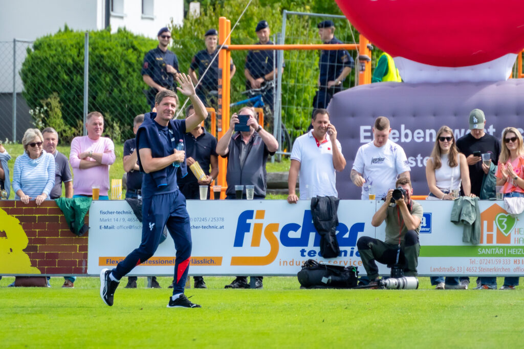 Fußballspiel auf einem Rasenplatz, am Rand Zuschauer und Zelte