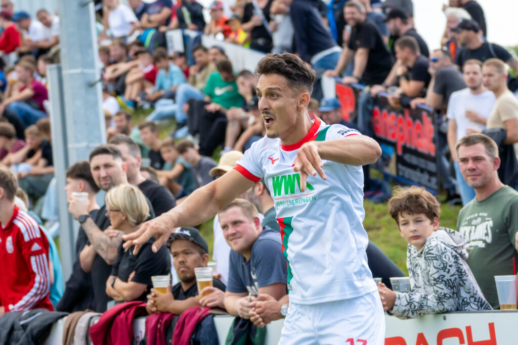 Spieler in rot-weißem Trikot am Spielfeldrand, im Hintergrund Fans