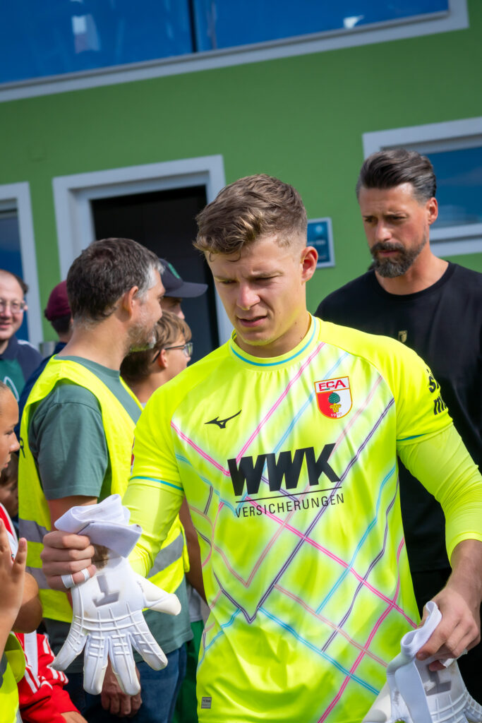 Torwart in grünem Trikot und gelben Handschuhen mit Mitspielern